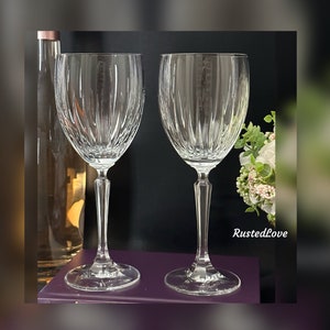 Pode incluir: Duas ta&ccedil;as de vinho de vidro transparente com um padr&atilde;o de nervuras verticais. As ta&ccedil;as est&atilde;o sobre uma superf&iacute;cie roxa.