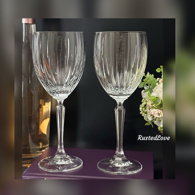 Pode incluir: Duas ta&ccedil;as de vinho de vidro transparente com um padr&atilde;o de nervuras verticais. As ta&ccedil;as est&atilde;o sobre uma superf&iacute;cie roxa.