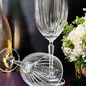 Pode incluir: Duas ta&ccedil;as de vinho de vidro transparente com um padr&atilde;o de nervuras verticais. As ta&ccedil;as est&atilde;o sobre um livro roxo com uma encaderna&ccedil;&atilde;o dourada.