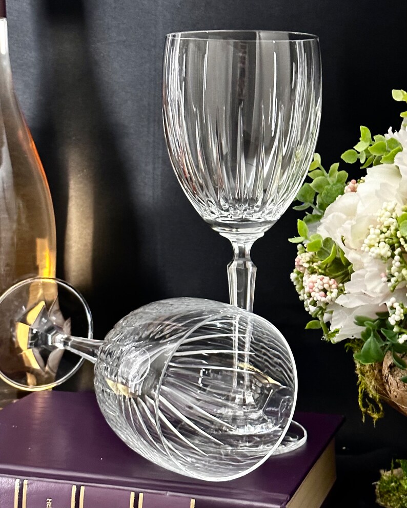 Pode incluir: Duas ta&ccedil;as de vinho de vidro transparente com um padr&atilde;o de nervuras verticais. As ta&ccedil;as est&atilde;o sobre um livro roxo com uma encaderna&ccedil;&atilde;o dourada.