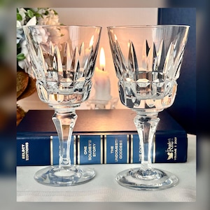 May include: Two clear glass wine glasses with a cut crystal design. The glasses are sitting on a book with the title "The Undomesticated Goddess" visible.