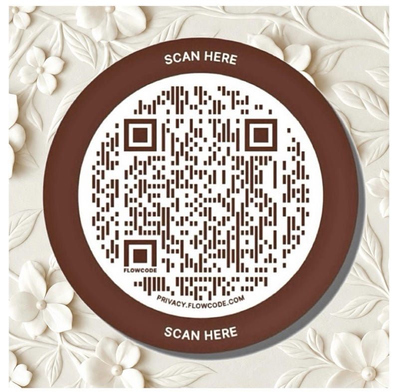 May include: A circular brown and white sign featuring a central QR code. The text SCAN HERE is printed at the top and bottom in white. The word FLOWCODE appears near the bottom left, and the URL PRIVACY.FLOWCODE.COM is printed at the bottom.