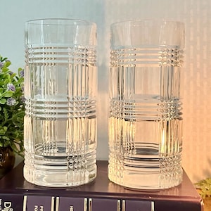 May include: Two clear glass tumblers with a geometric pattern. The glasses are tall and cylindrical with a square-shaped design.