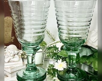 May include: Two clear, light green glass goblets featuring a distinct horizontal ribbed texture along the bowl. Each goblet has a sturdy stem and a wide, circular base, crafted from transparent green glass with a consistent ribbed pattern.