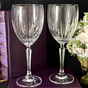 Pode incluir: Duas ta&ccedil;as de vinho de vidro transparente com um design de cristal cortado. As ta&ccedil;as est&atilde;o sobre um livro roxo com lombada dourada.