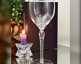 May include: A clear glass wine goblet featuring a smooth, rounded bowl with a thin silver rim at the top. The stem of the glass has a distinct twisted, spiral design that connects to a wide, flat circular base, providing stability for the vessel.