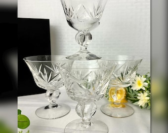 May include: A set of four clear crystal glasses featuring a wide bowl with intricate starburst cut patterns and a thick, rounded stem base. Each glass has a flared rim and a circular foot, showcasing a reflective, transparent glass construction.