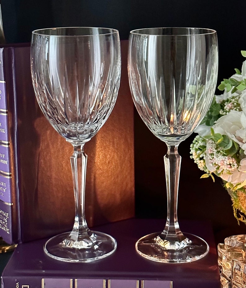 Pode incluir: Duas ta&ccedil;as de vinho de vidro transparente com um design de vidro cortado. As ta&ccedil;as est&atilde;o sobre uma superf&iacute;cie marrom.