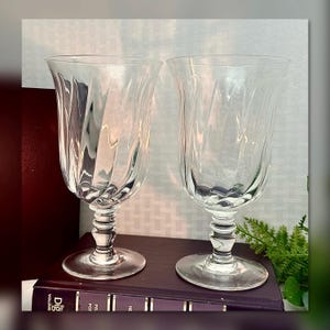 May include: Two clear glass goblets with a swirling, textured design. The goblets have a tall, slender stem and a wide, round bowl.