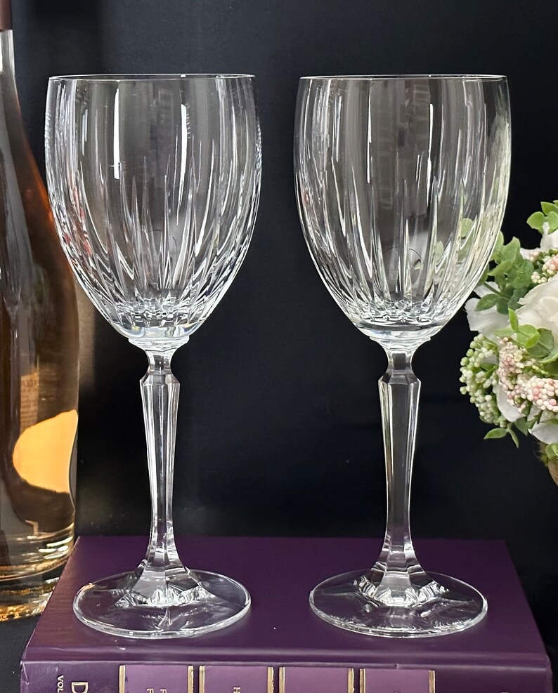 Pode incluir: Duas ta&ccedil;as de vinho de vidro transparente com um padr&atilde;o de nervuras verticais. As ta&ccedil;as est&atilde;o sobre uma superf&iacute;cie roxa.