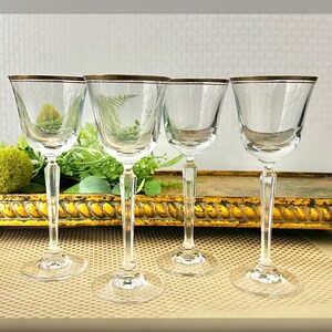 May include: Set of four clear glass wine glasses with a gold rim. The glasses have a tall, slender stem and a round bowl.