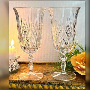 May include: Two clear crystal wine glasses with a cut glass design. The glasses have a tall, slender stem and a wide bowl.