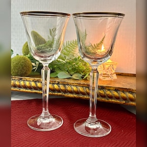 May include: Two clear glass wine glasses with a gold rim. The glasses have a tall, slender stem and a round bowl.