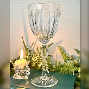 May include: A clear crystal wine glass with a long stem and a patterned bowl. The glass is positioned in front of a lit candle in a star-shaped holder and greenery.