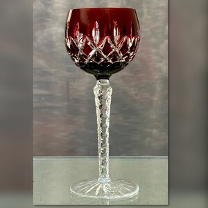 May include: A red wine glass with a clear, cut-glass stem and base. The bowl of the glass is decorated with a geometric pattern.