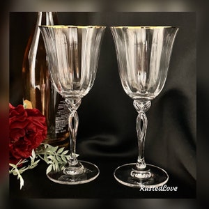 May include: Two clear glass wine glasses with gold rims. The glasses have a twisted stem and a wide bowl.