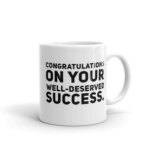 May include: White ceramic coffee mug with black text that reads "Congratulations on your well-deserved success."