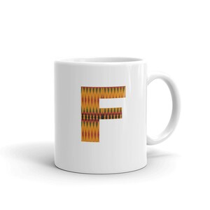 Può includere: Tazza in ceramica bianca con una grande lettera "F" stampata sul davanti. La lettera è in un motivo giallo, rosso, verde e nero.