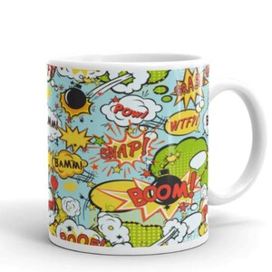 May include: White ceramic mug with a comic book style design. The mug features a light blue background with various comic book sound effects like "POW", "BOOM", and "SNAP". The design includes yellow stars, bombs, and speech bubbles.