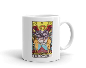 May include: White ceramic mug with a colorful illustration of The Lovers tarot card. The card features a winged figure above two nude figures standing on a landscape with a mountain. The text "VI THE LOVERS." is printed below the image.