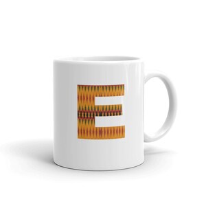 May include: White ceramic mug with a letter "E" printed on it. The letter is in a yellow, orange, red, green, and black pattern.
