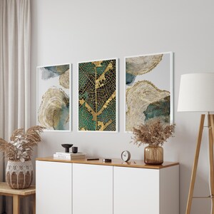 Puede incluir: Tres impresiones de arte abstracto enmarcadas con tonos dorados y verdes. La impresi&oacute;n central presenta un dise&ntilde;o de hoja de oro sobre un fondo verde. Las impresiones est&aacute;n colgadas en una pared blanca sobre un armario blanco.