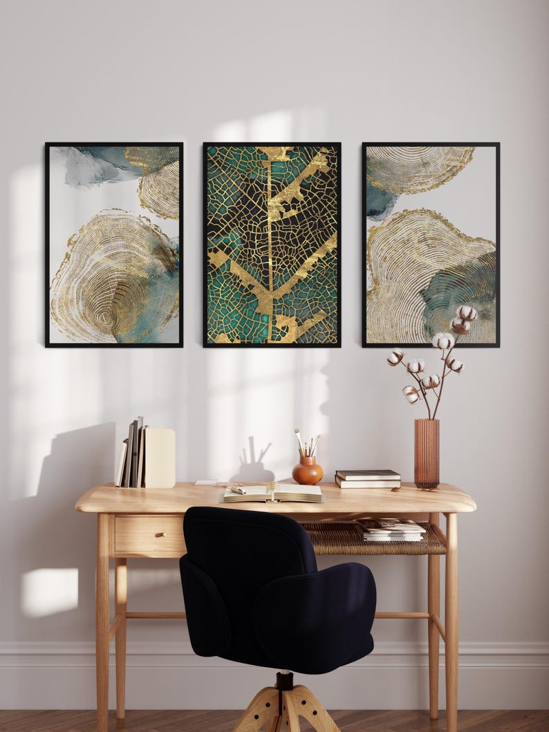 Puede incluir: Tres impresiones de arte abstracto enmarcadas con colores dorados y verdes. La impresi&oacute;n central presenta un dise&ntilde;o de hoja de oro sobre un fondo verde. Las impresiones est&aacute;n colgadas en una pared blanca sobre un escritorio de madera con una silla negra.