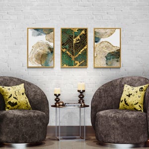 Puede incluir: Tres impresiones de arte abstracto enmarcadas con acentos dorados y verdes. Las impresiones est&aacute;n colgadas en una pared de ladrillo blanco sobre dos sillones de terciopelo marr&oacute;n con almohadas amarillas con un patr&oacute;n de Halloween.