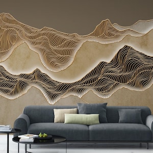 May include: A contemporary living room with a dark grey sofa, cushions, and a black coffee table. The wall features a large mural of abstract mountain ranges with gold wave-like lines on a neutral background. The room has a modern aesthetic.