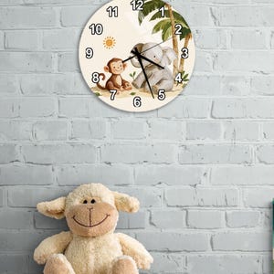 Könnte beinhalten: Eine runde Wanduhr mit cremefarbenem Zifferblatt und schwarzen Ziffern von 1 bis 12. Das Motiv zeigt einen braunen Affen und einen grauen Elefanten auf einem Sandstrand mit Palmen und einer kleinen gelben Sonne. Schwarze Uhrzeiger sind mittig.