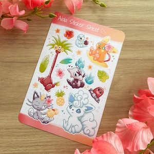 May include: A sticker sheet with a colourful tropical theme featuring various Pokemon characters from the Alola region. The sheet includes a palm tree, a surfing Vaporeon, a Rockruff, a Mimikyu, and a Rowlet. The text "Alola Sticker Sheet" is printed at the top of the sheet.