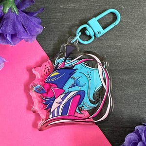 May include: A blue and pink anime character keychain with a black and white design. The keychain is made of clear acrylic and has a silver metal ring.