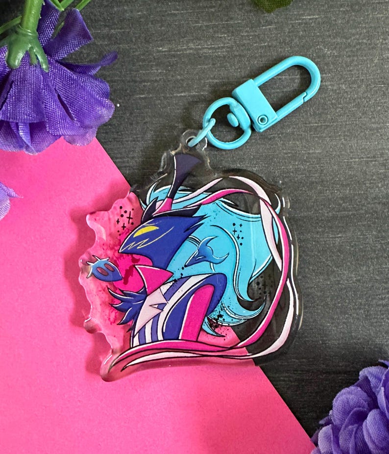 May include: A blue and pink anime character keychain with a black and white design. The keychain is made of clear acrylic and has a silver metal ring.