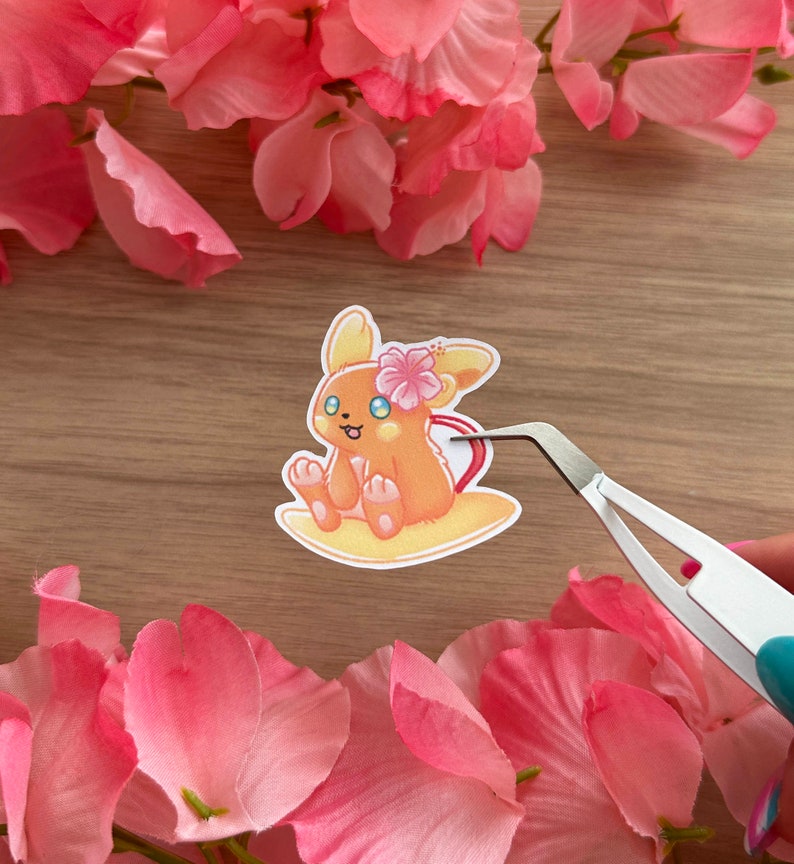 May include: A sticker featuring a cartoon illustration of a small, orange, fox-like Pokemon with a pink flower on its head. The Pokemon is sitting on a yellow surfboard.