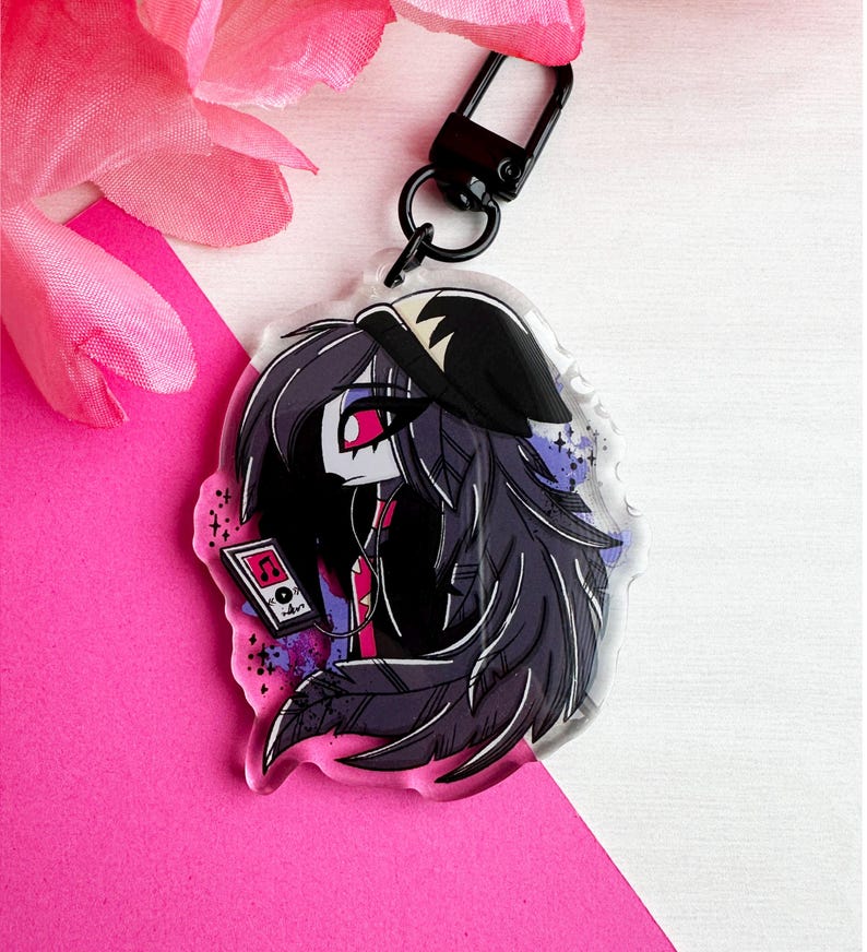 May include: A clear acrylic keychain featuring a cartoon character with long black hair, wearing a black hat and a red shirt. The character is holding a small music player with a play button. The background is a purple and blue gradient with white stars.