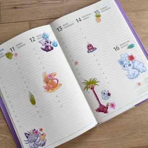 May include: A weekly planner with colourful stickers of cartoon characters. The stickers feature a variety of characters, including a pink and yellow character with a flower crown, a blue and white character with a flower crown, and a green character with a flower crown. The planner has a purple cover and is open to the week of June 11th to June 17th.