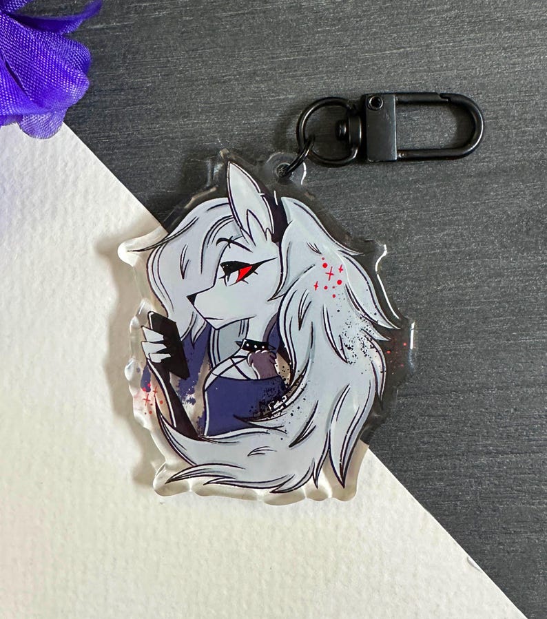 May include: A white and gray anime character with red eyes and black hair holding a black phone. The character is on a clear acrylic keychain with a black metal ring.