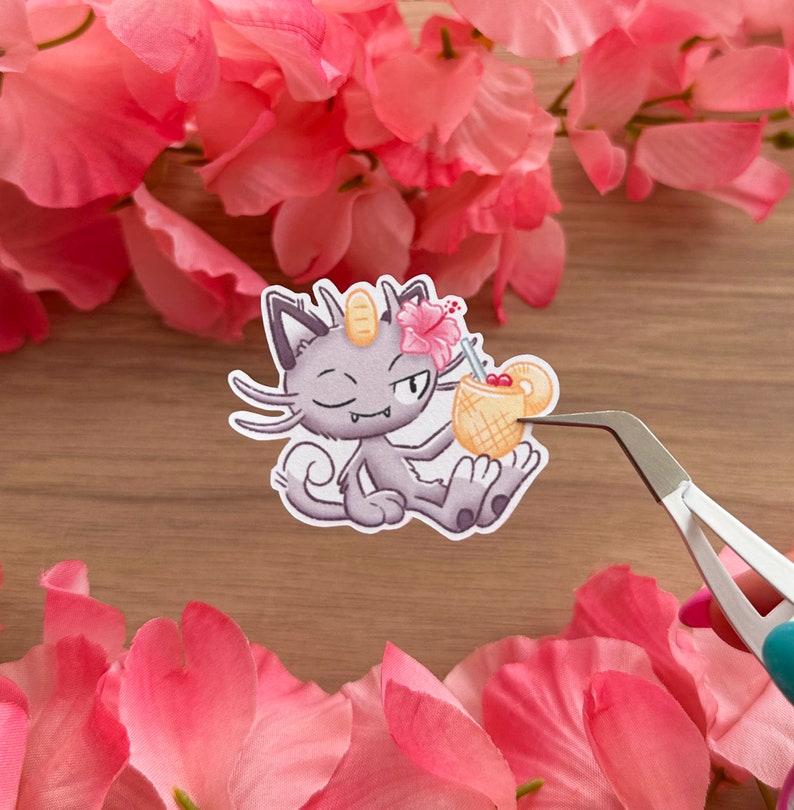 May include: A sticker featuring a cartoon purple cat with a winking eye holding a yellow pineapple drink with a pink flower on top. The sticker is on a wooden surface.