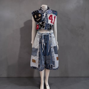 May include: A sleeveless denim waistcoat featuring a white lace-up front, a red number 41 patch, and a black circular face graphic, paired with knee-length denim shorts constructed from light and dark blue panels with multiple pockets and white drawstrings.