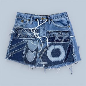 Könnte beinhalten: Minirock aus Jeansstoff mit Patchwork-Design. Der Rock hat verschiedene Blautöne, dekorative Patches, ausgefranste Kanten und einen weißen Kordelzug. Der Rock hat ein einzigartiges, handgefertigtes Aussehen.