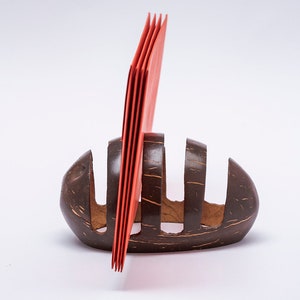 May include: A brown coconut shell holder with four slots for holding red envelopes. The holder is made from a natural coconut shell and has a rustic, handmade look.