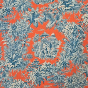 Könnte beinhalten: Ein leuchtend orangefarbener Stoff mit einem detaillierten blau-weißen Toile-de-Jouy-Muster. Das Muster zeigt einen Elefanten mit Figuren, umgeben von Palmen, Tempeln und tropischem Laub. Das Thema ist eine exotische Landschaft.
