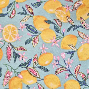 Può includere: Un tessuto azzurro con un motivo ripetuto di limoni gialli, fiori rosa e foglie verdi e blu. Alcuni limoni sono interi, altri sono tagliati. Il design è una stampa allegra ed estiva.