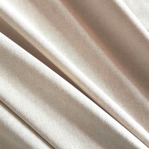 May include: Close-up of a smooth, off-white fabric with a subtle texture. The fabric is folded and draped, creating soft folds and curves.