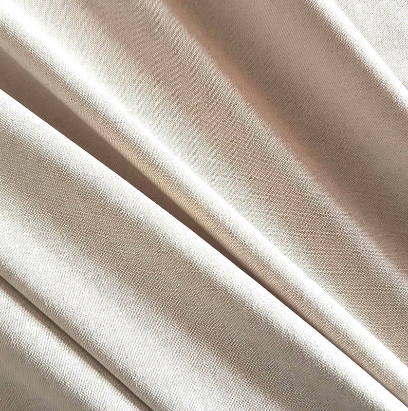 May include: Close-up of a smooth, off-white fabric with a subtle texture. The fabric is folded and draped, creating soft folds and curves.