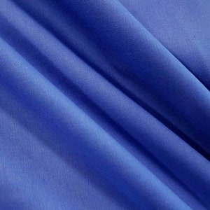 Op de afbeelding: Een close-up van een gladde, blauwe stof met een subtiele textuur. De stof is gevouwen op een manier die zachte, vloeiende lijnen creëert.