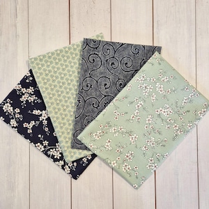 Può includere: Quattro quadrati di tessuto piegati con disegni floreali e fantasia. I tessuti presentano un blu navy con fiori bianchi, un verde chiaro con un motivo ripetuto, un blu scuro con un motivo a spirale e un verde chiaro con fiori bianchi.