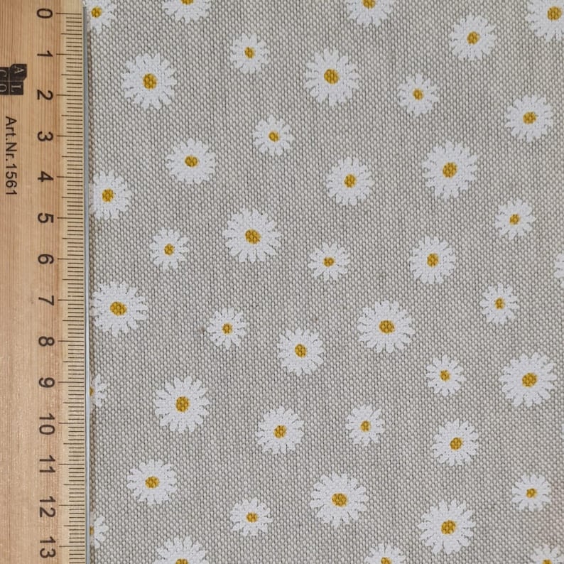 May include: A close-up of a light grey fabric with a white daisy pattern. The daisies have yellow centres.
