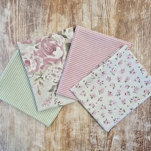 Könnte beinhalten: Eine Sammlung von Stoffquadraten mit verschiedenen Blumen- und Streifenmustern. Die Stoffe weisen Farbtöne von Rosa, Grün und Creme auf. Ein Stoff hat große rosa Rosen, ein anderer kleine rosa Blüten.