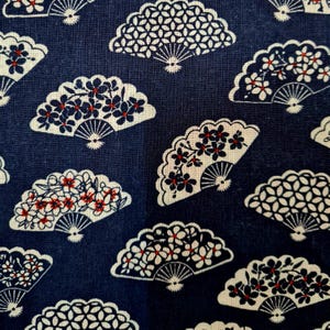 Può includere: Un tessuto blu navy con un motivo ripetuto di ventagli bianchi e rossi. I ventagli sono decorati con piccoli fiori bianchi e centri rossi.